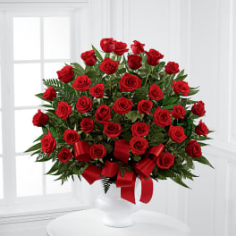 Red roses arranged in a white vase with a red ribbon