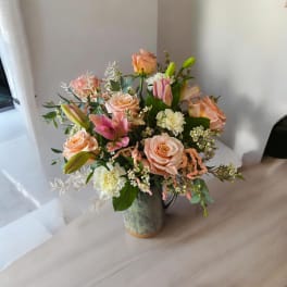 Peach roses and pink lilies arranged in a ceramic pitcher vase