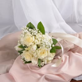 Hand-tied bouquet of ivory roses and white flowers with ribbon on pink fabric