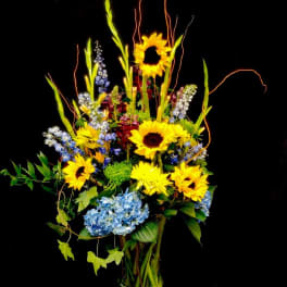 Tall bouquet of sunflowers and blue hydrangeas in a clear glass vase