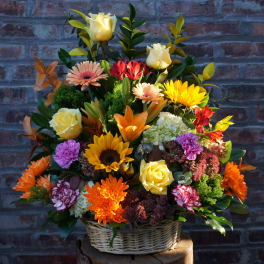 Mixed flower arrangement in a wicker basket with yellow roses and bright daisies
