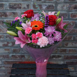 Mixed bouquet of pink, red, and orange flowers wrapped in purple paper