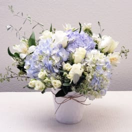 White and pale blue flowers arranged in a white vase.