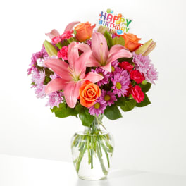Pink lilies and mixed flowers in a glass vase with a Happy Birthday pick