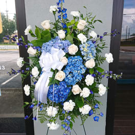 Standing floral spray with blue hydrangeas, white roses, and a white ribbon