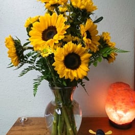 Sunflower bouquet in a clear glass vase beside a glowing salt lamp