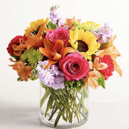 Mixed bouquet of roses, sunflowers, lilies, and carnations in a glass vase