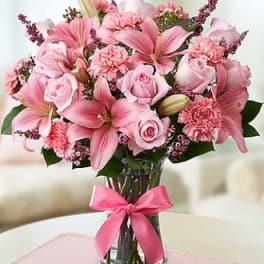 Pink lilies and roses arranged in a glass vase with a pink ribbon