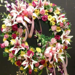 Heart-shaped floral wreath with pink lilies, roses, and ribbons
