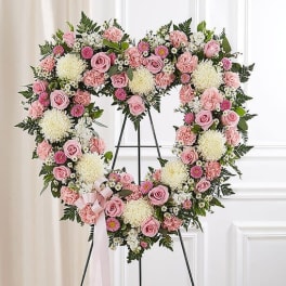 Heart-shaped floral wreath with pink roses and white blooms on a stand