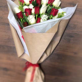 Hand-tied bouquet of red and white roses wrapped in kraft paper with a red ribbon