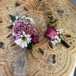 Pink and white corsage and boutonniere set on a carved wooden table