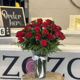 Tall bouquet of red roses in a clear glass vase with a white ribbon bow.