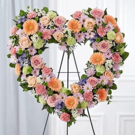 Heart-shaped floral wreath on an easel with pink, peach, and lavender blooms