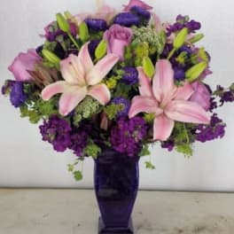 Pink lilies and purple flowers arranged in a tall purple vase