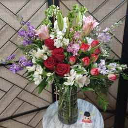 Mixed bouquet of red roses, pink tulips, lilies, and purple flowers in a glass vase