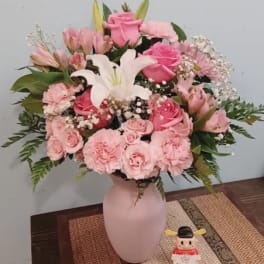 Pink and white floral arrangement in a pale vase with a small figurine beside it