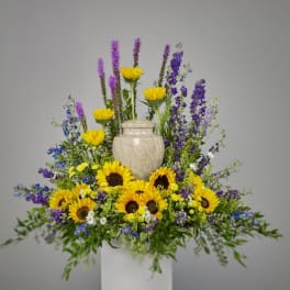 Cremation floral display with yellow sunflowers and purple blooms surrounding a stone urn