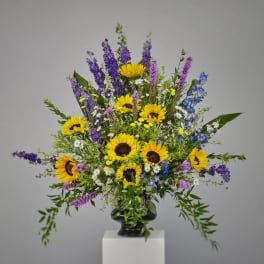 Tall arrangement of yellow sunflowers with purple and blue flowers in a black urn vase