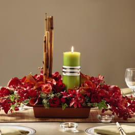 Low red floral centerpiece with green pillar candle and bamboo sticks on a set dining table