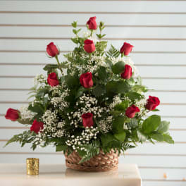 Basket arrangement of red roses and white filler flowers in a woven basket.