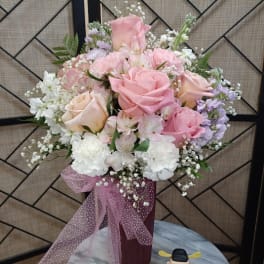 Pink and white rose bouquet in a burgundy vase with a pink ribbon