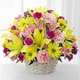 Yellow lilies and daisies with pink carnations in a white wicker basket