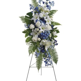 Tall standing spray of white lilies and roses with blue flowers on a metal easel