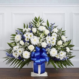 Tall white and blue floral arrangement with a large blue bow in a white container