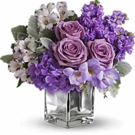 Purple roses and mixed lavender flowers in a clear glass vase
