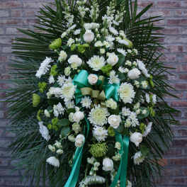 White floral standing spray with teal ribbons against a brick wall