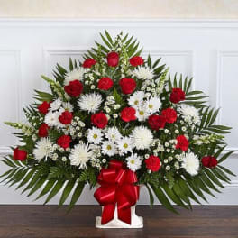 Red and white floral standing spray with a red ribbon on a white base