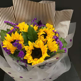 Bouquet of yellow sunflowers with purple filler flowers in striped wrap