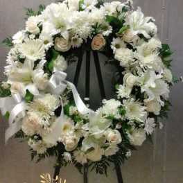 White floral wreath on a black easel with a ribbon bow