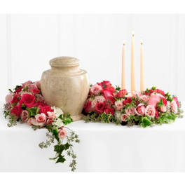 Cremation urn framed by pink and red rose arrangements with three ivory taper candles
