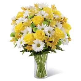 Yellow roses, white daisies, and green button mums arranged in a clear glass vase