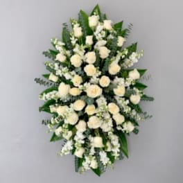 Oval spray of white roses and white flowers arranged over dark foliage