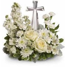 Low white floral arrangement with roses and daisies surrounding a silver cross ornament