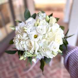 Hand-tied bouquet of white roses, lisianthus, and hydrangea with dark green accents
