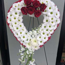 Heart-shaped floral wreath with red roses and white daisies on a stand