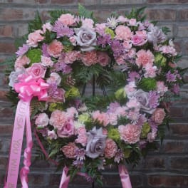 Heart-shaped floral wreath with pink and lavender flowers on a brick wall