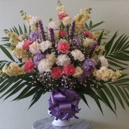Mixed bouquet of carnations and roses in a white vase with a purple ribbon