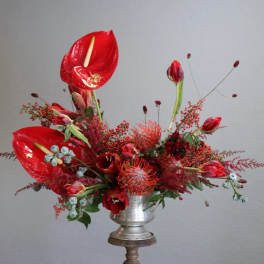 Red floral arrangement in a silver pedestal vase with tall tropical blooms