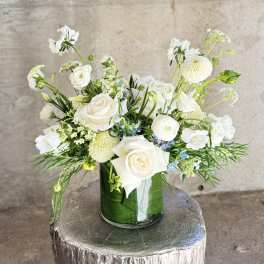 White floral arrangement in a glass vase with roses and round blooms