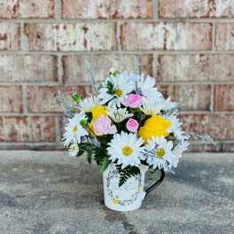 Bouquet of white daisies and yellow and pink roses in a white mug vase