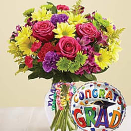 Bright mixed bouquet in a glass vase with a colorful Congrats Grad balloon