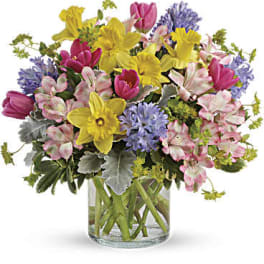 Mixed bouquet of yellow daffodils, pink tulips, and purple flowers in a glass vase