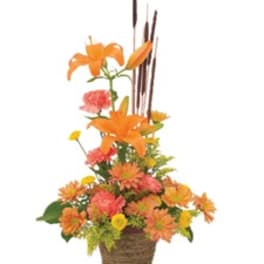 Orange and pink floral arrangement in a woven basket with tall reeds