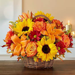 Basket arrangement of sunflowers, orange roses, and red daisies