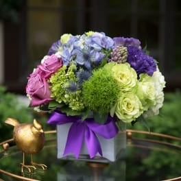Colorful bouquet in a square vase with a purple ribbon